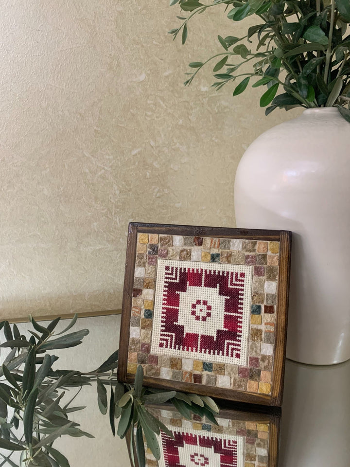 Framed mosaic art piece on a surface with a plant and vase in the background