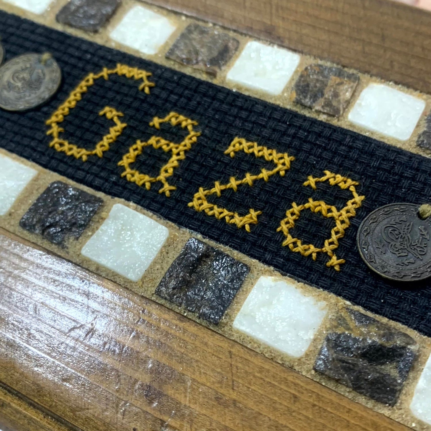 Embroidered patch with 'Ud28' in yellow on a black background, attached to a wooden surface.